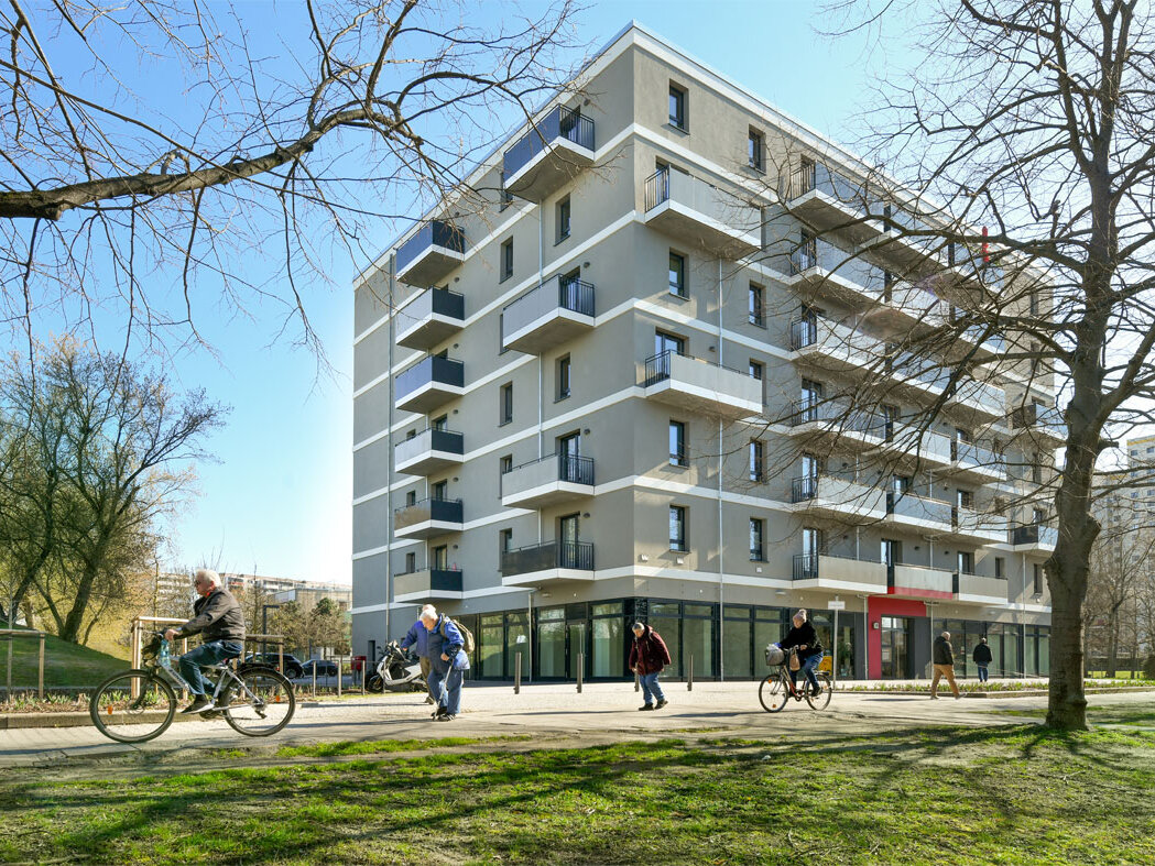 Außenansicht degewo-Neubau Mehrower Allee 28 und 30 mit Rasenfläche im Vordergrund und Weg, auf dem Personen gehen und Fahrrad fahren.