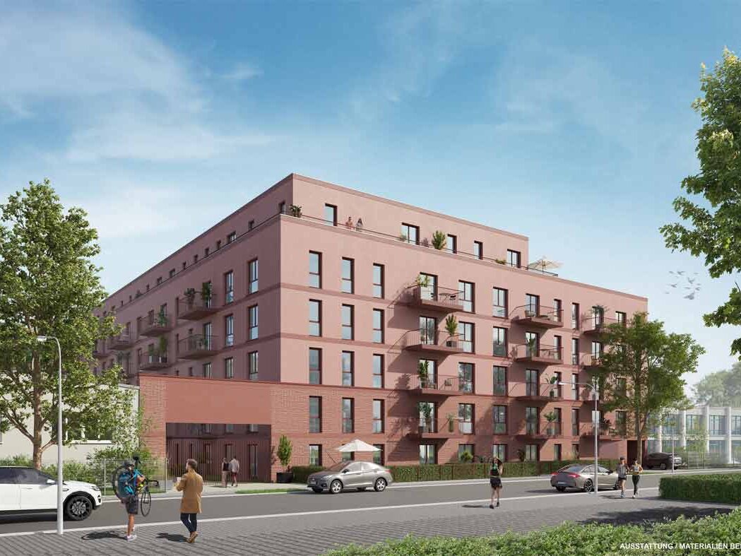 Straßenansicht des Mehrfamilienhauses mit roter Fassade, Staffelgeschoss und Balkonen. Vor dem Gebäude verlaufen Gehweg und Fahrbahn.