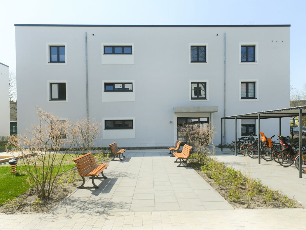 Außenansicht degewo-Neubau Rudower Straße 47 bis 51: Hofseite mit Spielplatz, Sitzbänken und überdachten Fahrradständern.