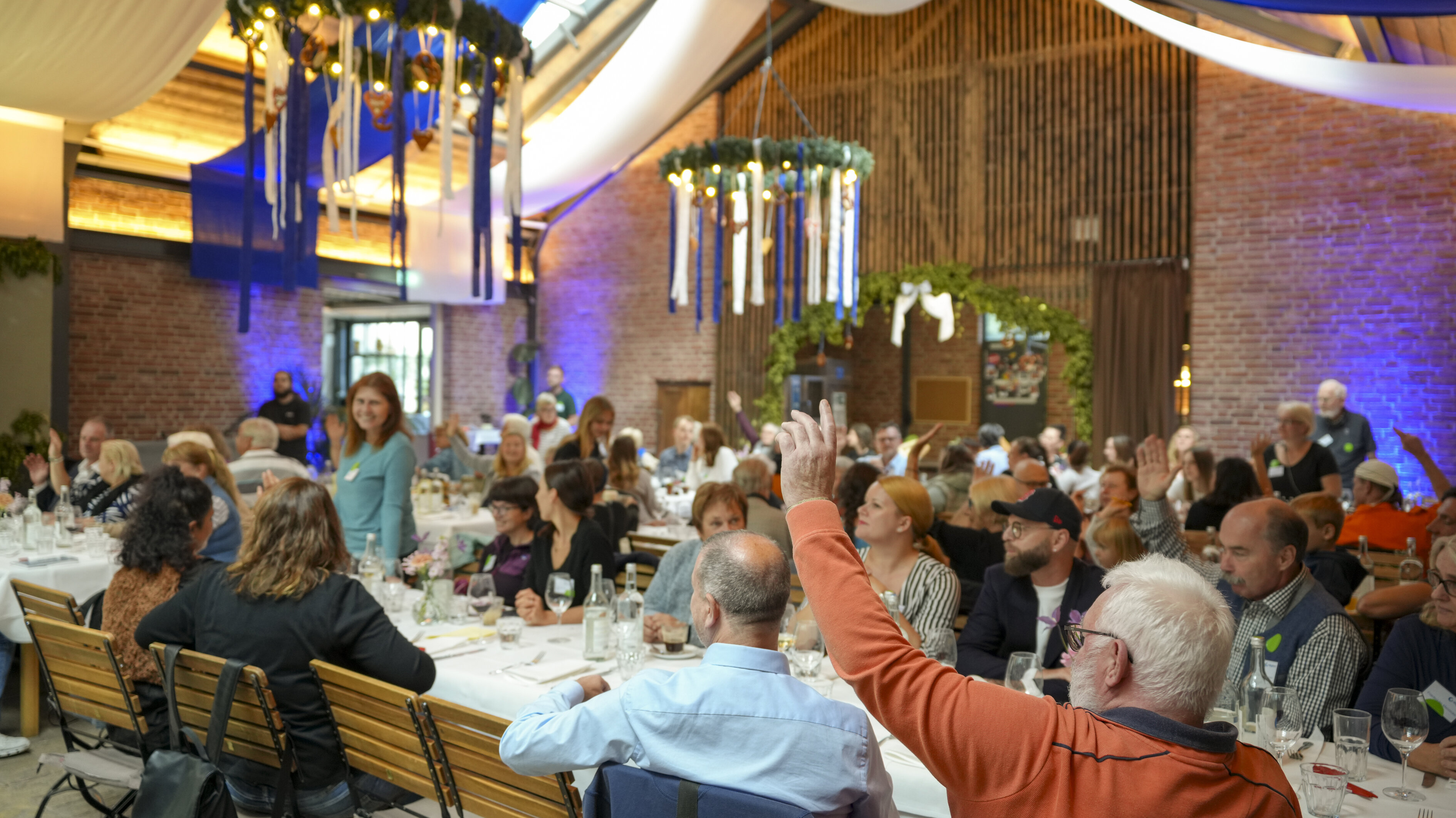 Große Gruppe sitzt an langen Tischen bei Veranstaltung.