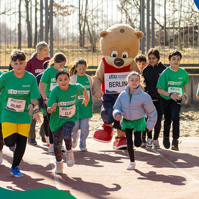 Eine Gruppe Kinder rennt auf einem Sportplatz mit dem Maskottchen Berlino.
