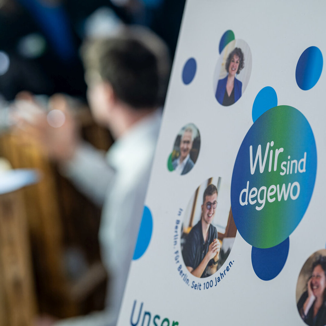 Aufsteller mit Schriftzug Wir sind degewo. Im Hintergrund sind Menschen zu sehen, die ein Foto machen. 