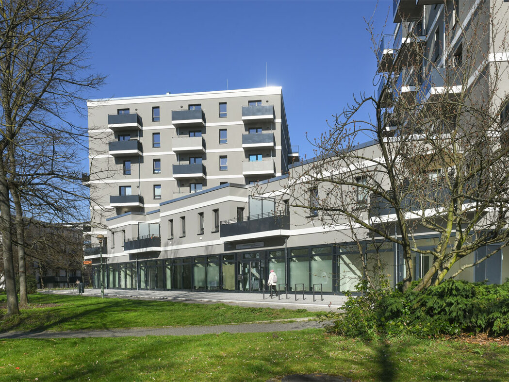 Außenansicht degewo-Neubau Mehrower Allee 28 und 30 mit Rasenflächen, Wegen und Bäumen im Vordergrund.