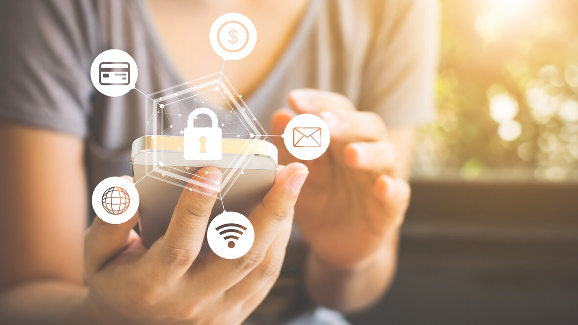 Person hält ein Smartphone in der Hand. Über dem Gerät sind Symbole für Sicherheit, WLAN, E-Mail, Kreditkarte und Internet mit einem Schloss dargestellt.