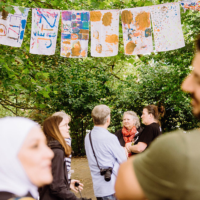 Einige Menschen stehen auf dem Apfelsinenplatz in Gropiusstadt und unterhalten sich