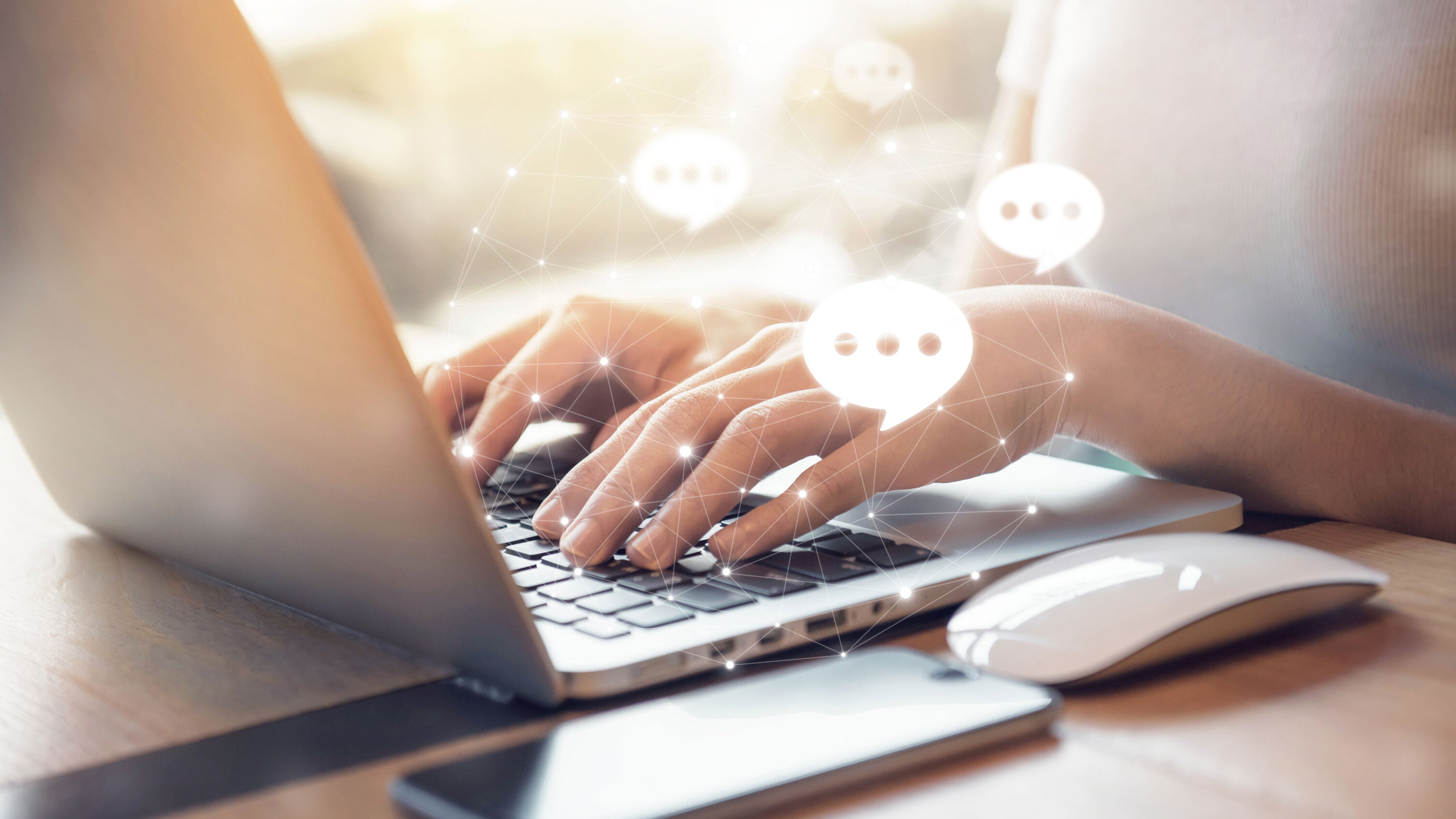 Hände tippen auf einer Laptop-Tastatur, daneben Smartphone und Maus; eingeblendete Chat-Symbole stehen für digitalen Kundenservice und Online-Kommunikation.