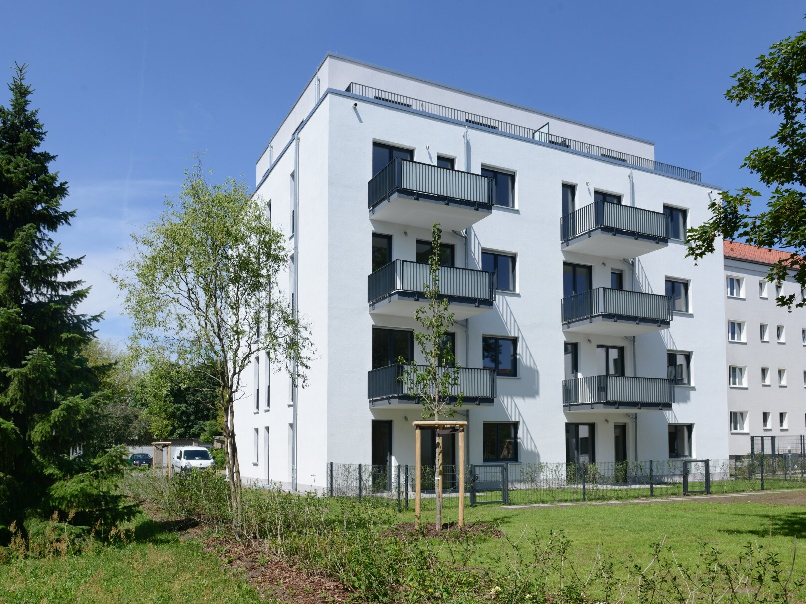 Außenansicht degewo-Neubau Klutstraße 22c mit Bäumen, Beeten und Rasenflächen im Vordergrund.