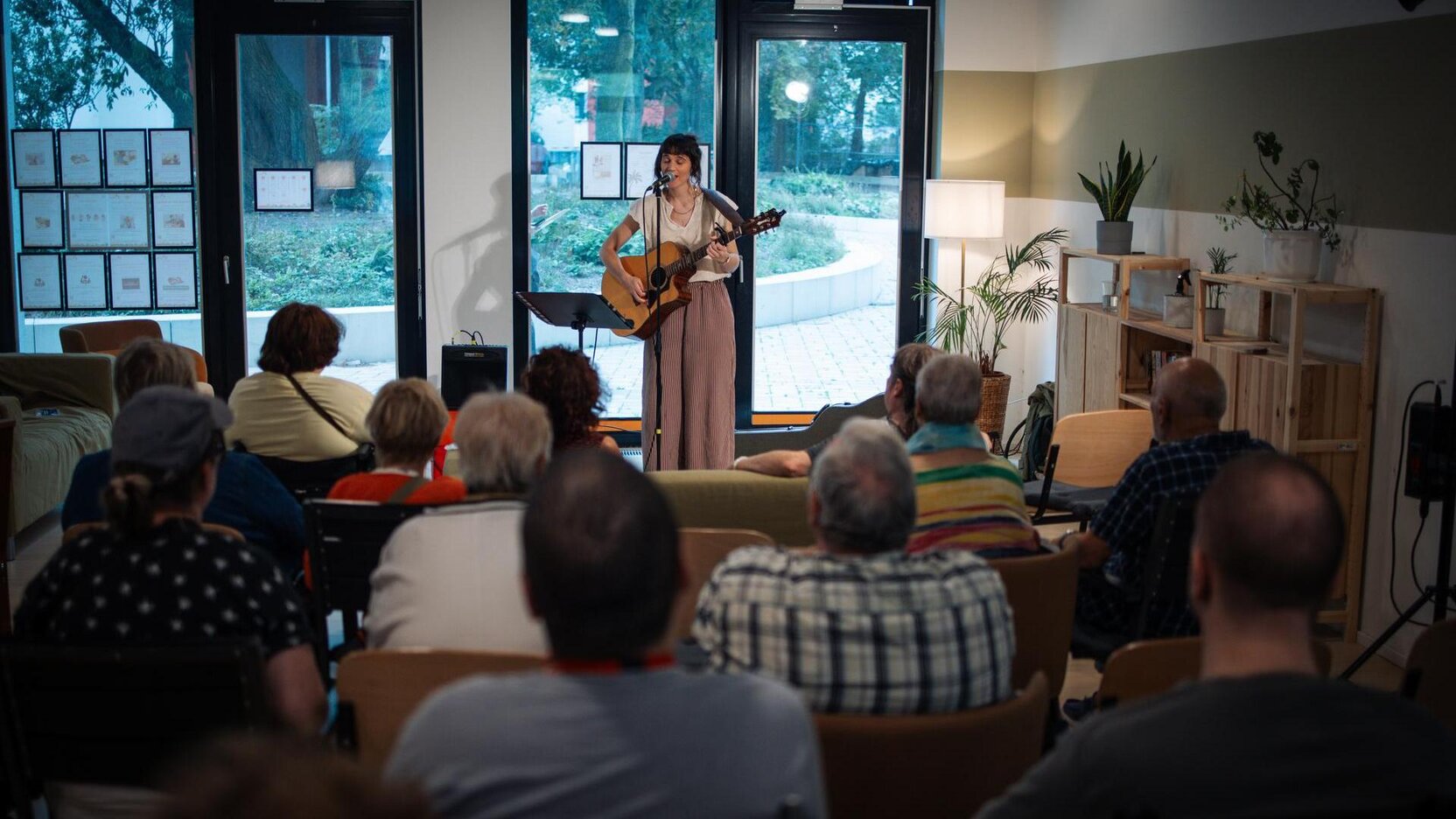 Eine Musikerin steht mit einer Gitarre auf einer Bühne und spielt für ein älteres Publikum. 