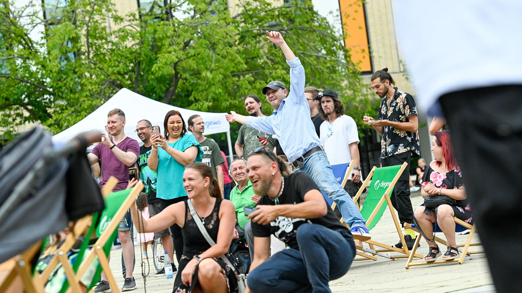 Menschen sitzen auf Stühlen vor einer Open Air Bühne und genießen das Programm. Sie tanzen und jubeln.