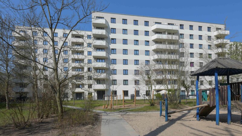 Außenansicht degewo-Neubau Wuhlestraße 2 bis 8 mit Bäumen, Weg und Spielplatz im Vordergrund.