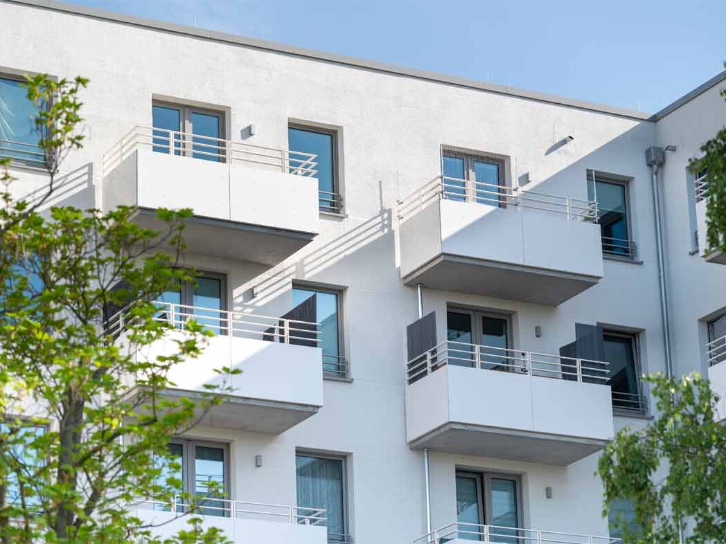 Außenansicht degewo-Neubau Pechsteinstraße 64b: Fassade mit Balkonen sowie links und rechts beblätterten Bäumen im Vordergrund.