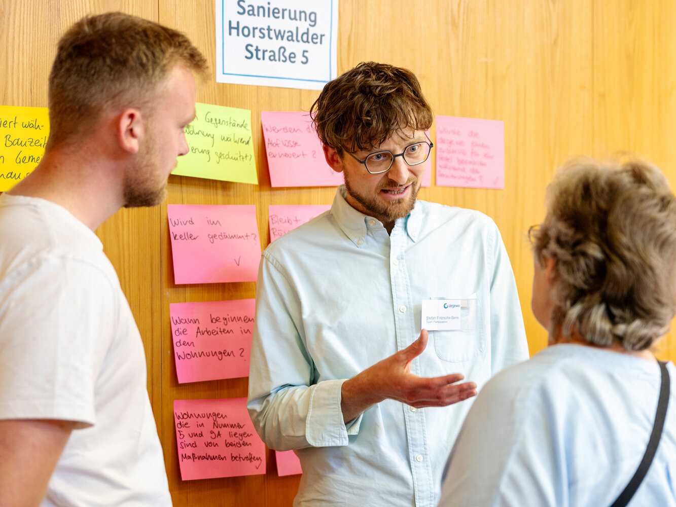 Ein degewo-Mitarbeiter erläutert Fragen zur Sanierung im direkten Gespräch mit Bewohnenden. Im Hintergrund sind Haftnotizen mit Fragen und Anmerkungen zu sehen.