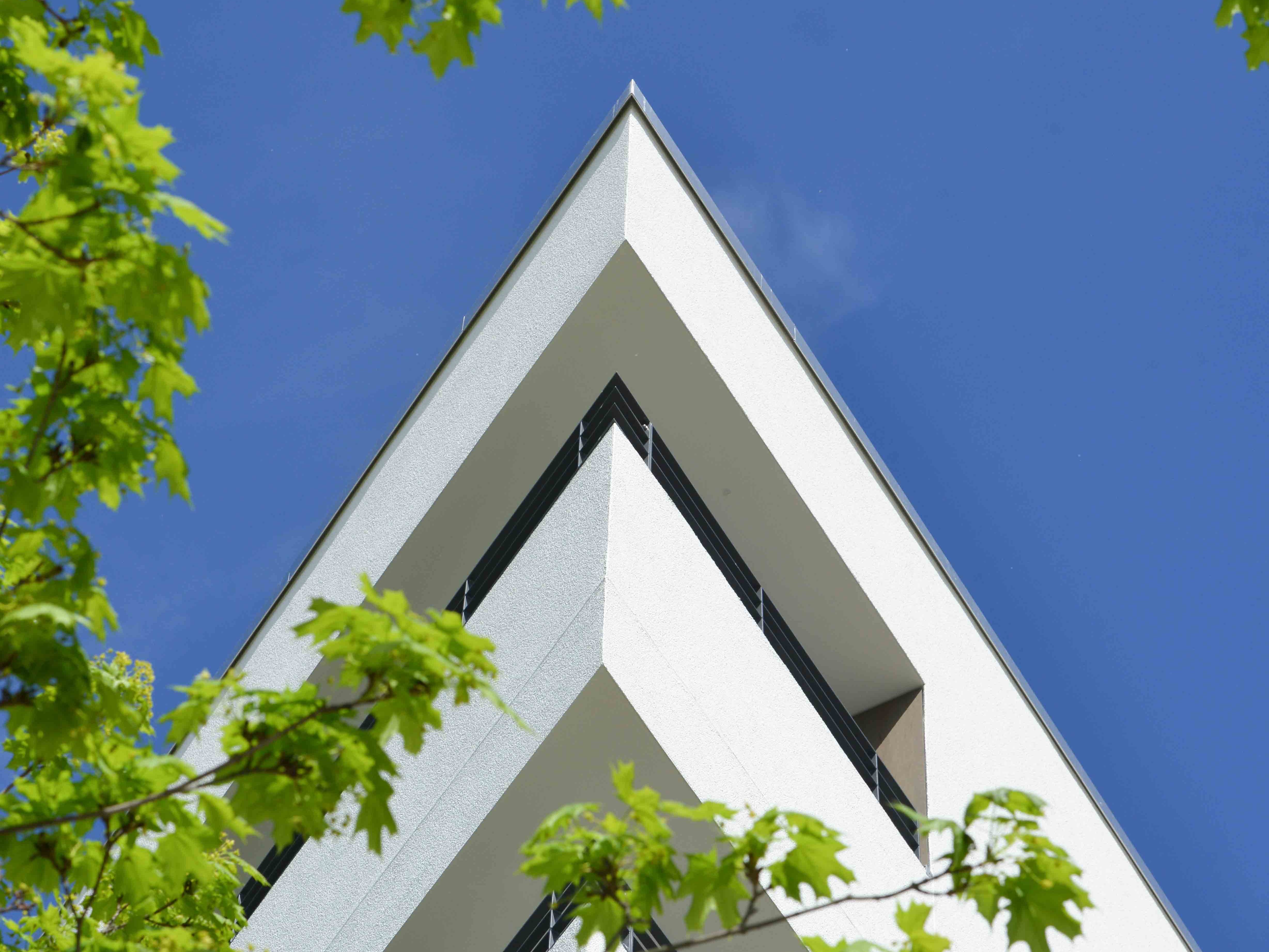 Außenansicht Eckbalkone degewo-Neubau Joachim-Ringelnatz-Straße Cecilienstraße 191 mit beblätterten Baumzweigen im Vordergrund.