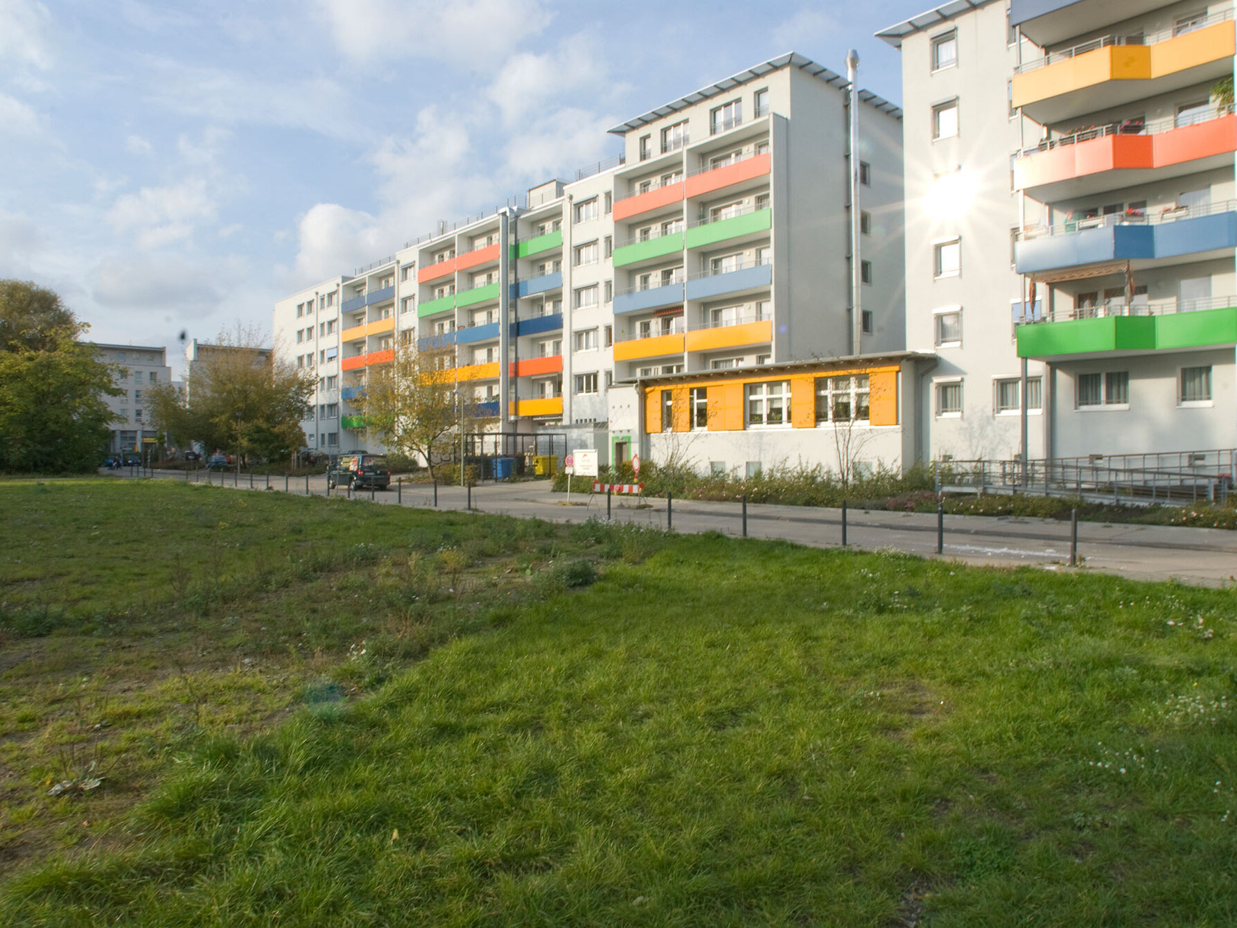 Mehrere modernisierte Wohnhäuser mit farbigen Balkonbrüstungen in Grün, Gelb, Blau und Orange, davor eine Grünfläche und ein Gehweg.