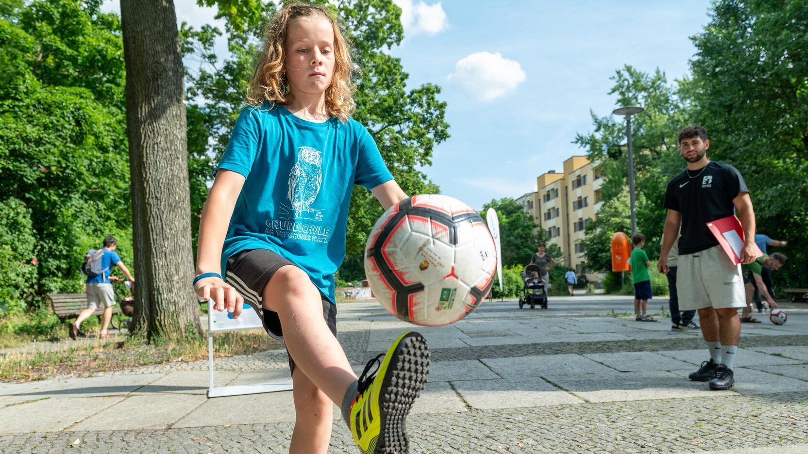 Ein Junge schießt den Bild, im Hintergrund schaut der Coach zu.