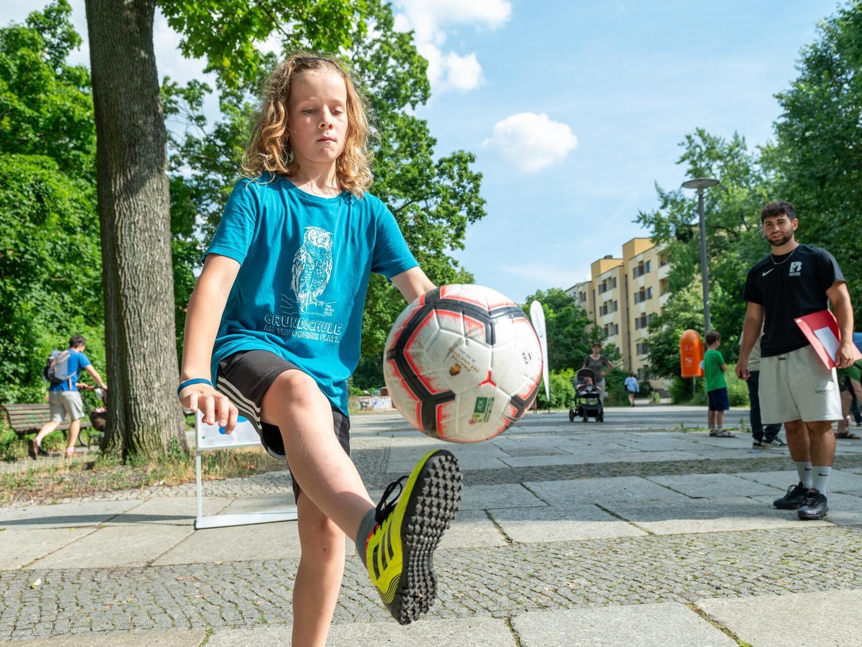 Ein Junge schießt den Bild, im Hintergrund schaut der Coach zu.