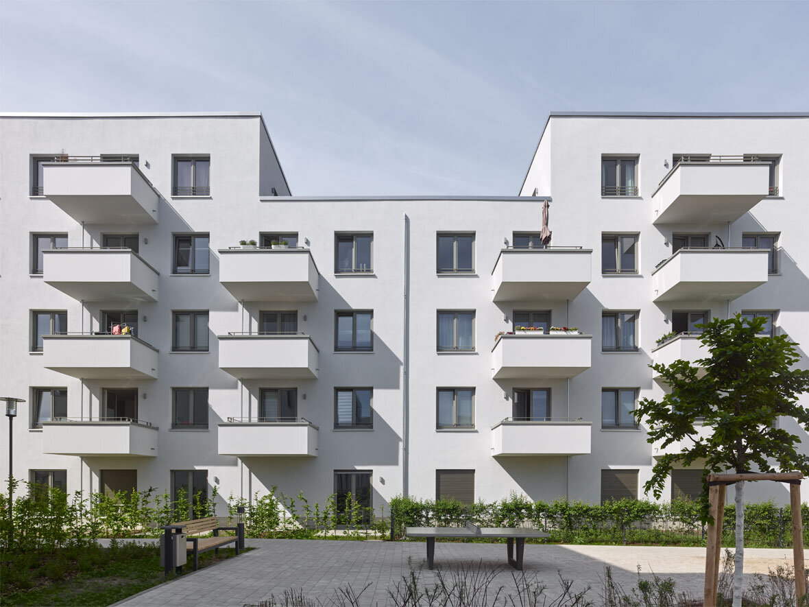 Außenansicht degewo-Neubau Dessauerstraße 39 bis 45 a-b Retzowstraße 54 bis 60: Hofseite mit Sitzbank, Tischtennisplatte und rechts neu gepflanztem Baum sowie Sträuchern im Vordergrund.