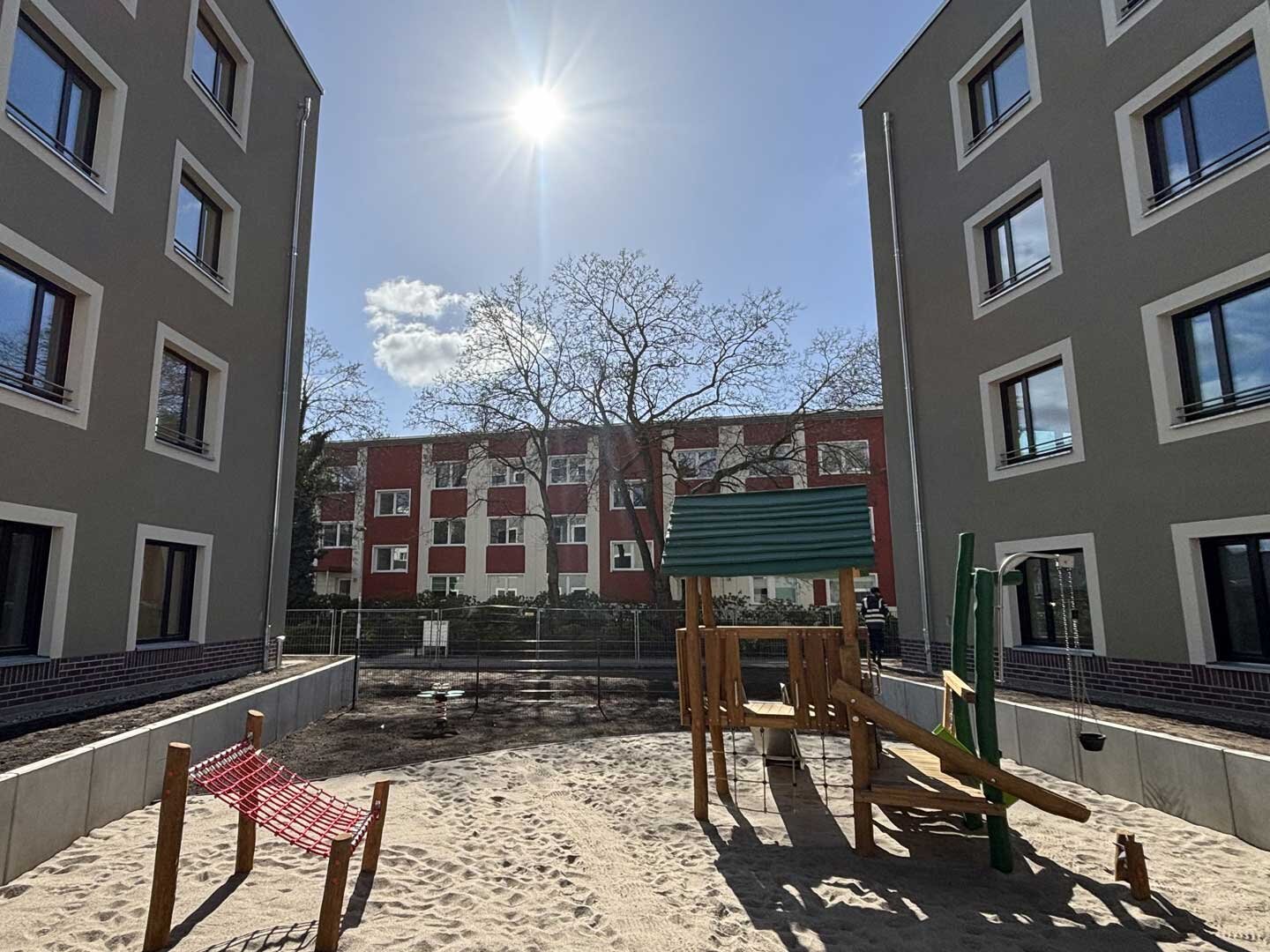 Ansicht eines Spielplatzes zwischen zwei Gebäuden mit Klettergerüst und einem weiteren Spielgerät.