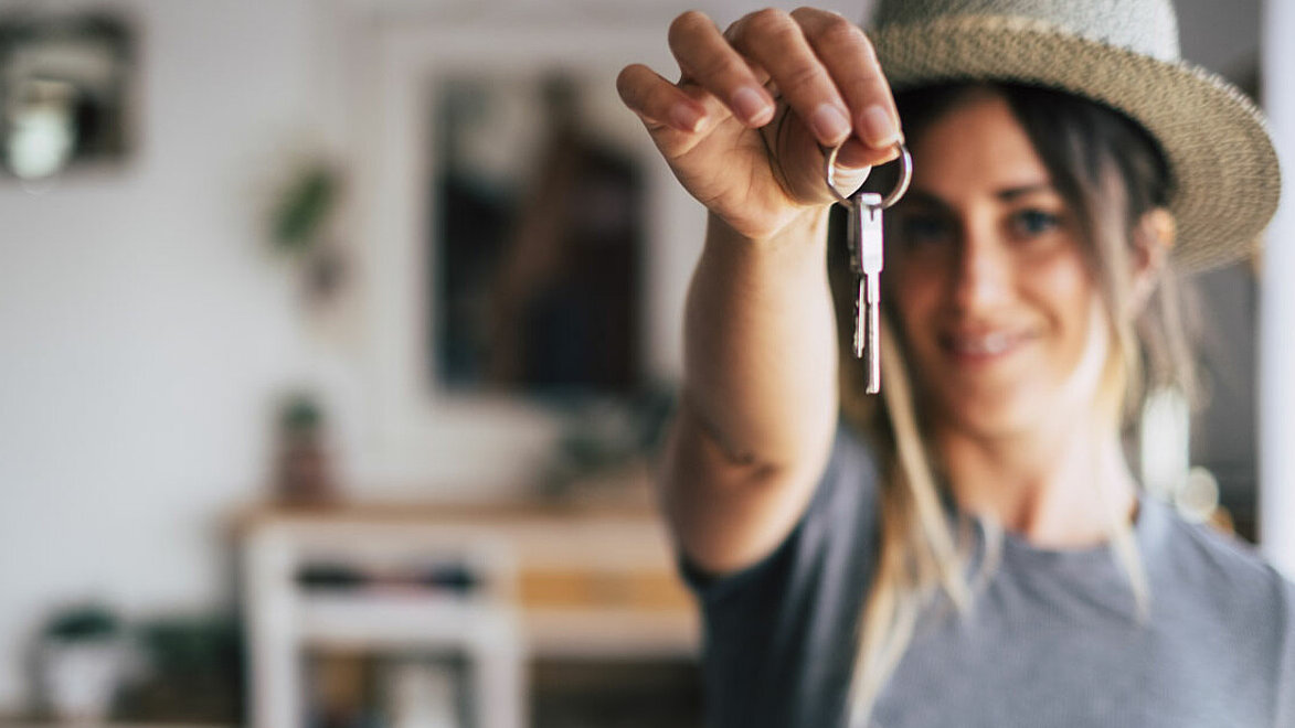 Eine Frau zeigt ihren Schlüssel der neuen Wohnung in die Kamera