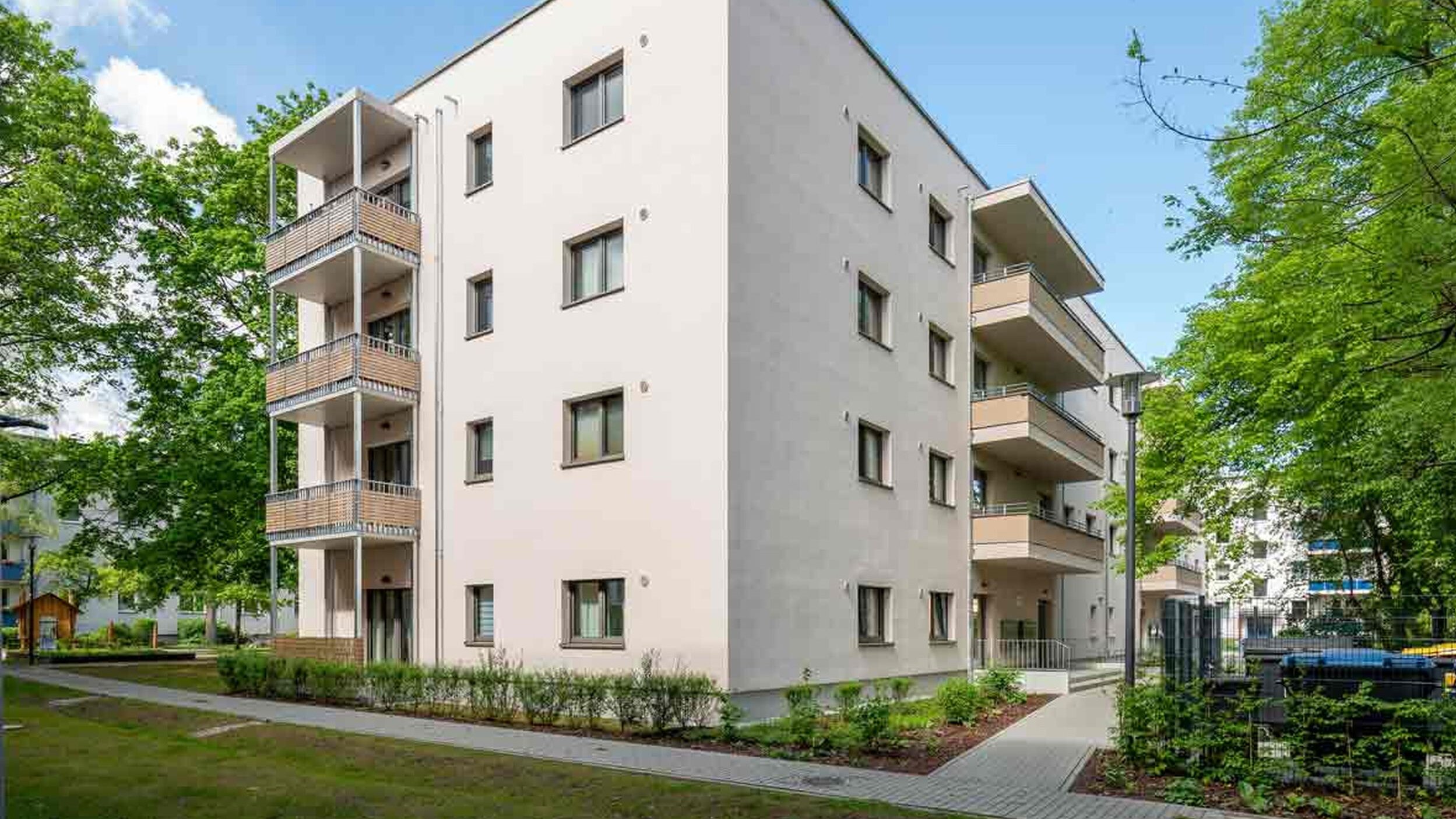 Außenansicht degewo-Neubau Färberstraße 19A mit Grünflächen, Wegen und beblätterten Bäumen im Vordergrund.