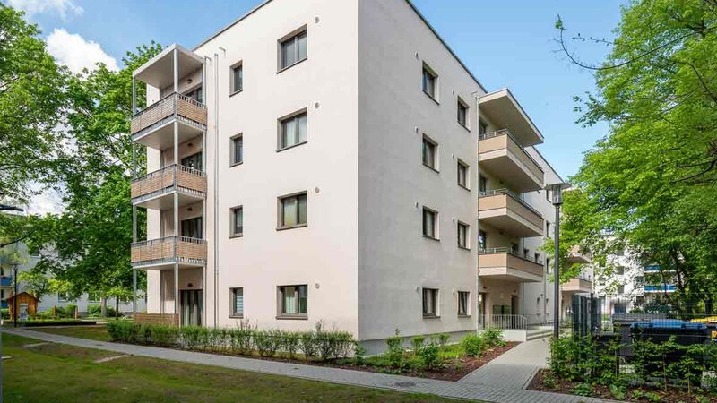 Außenansicht degewo-Neubau Färberstraße 19A mit Grünflächen, Wegen und beblätterten Bäumen im Vordergrund.