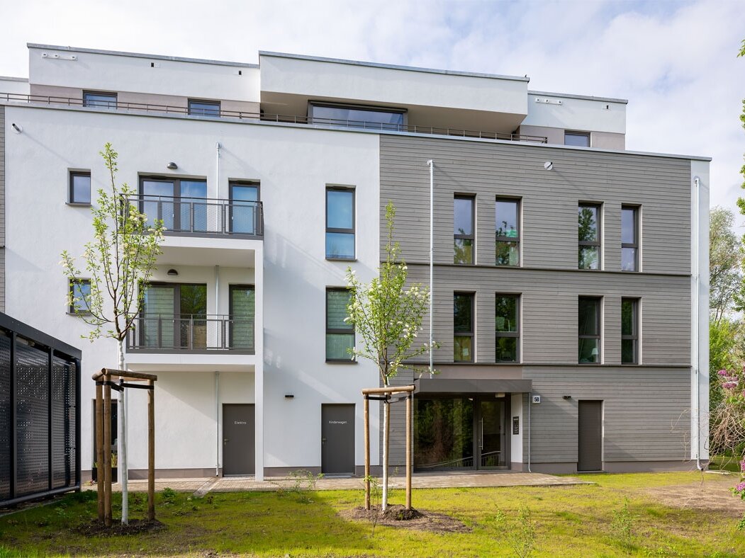 Außenansicht degewo-Neubau Stillerzeile 58 mit Grünfläche und neu gepflanzten Bäumen davor.