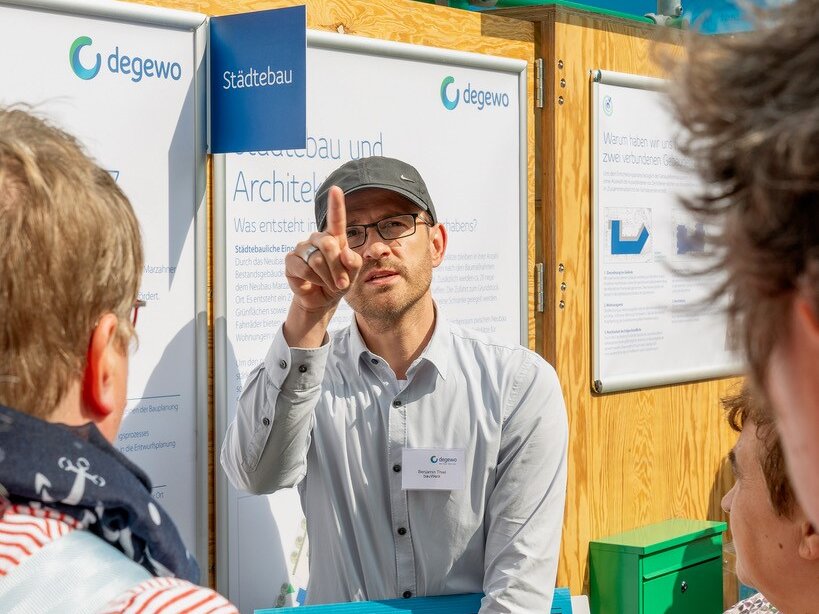 degewo-Mitarbeiter im Gespräch mit Anwohnenden an der Dialogstation, erläutert Planungsinhalte anhand ausgestellter Informationstafeln.