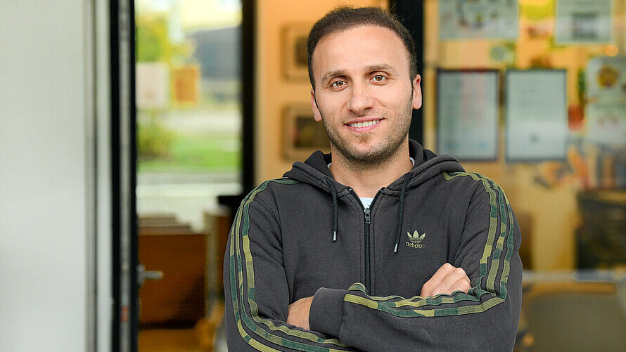 Ein Mann steht im Eingang eines Cafés und lächelt in die Kamera.