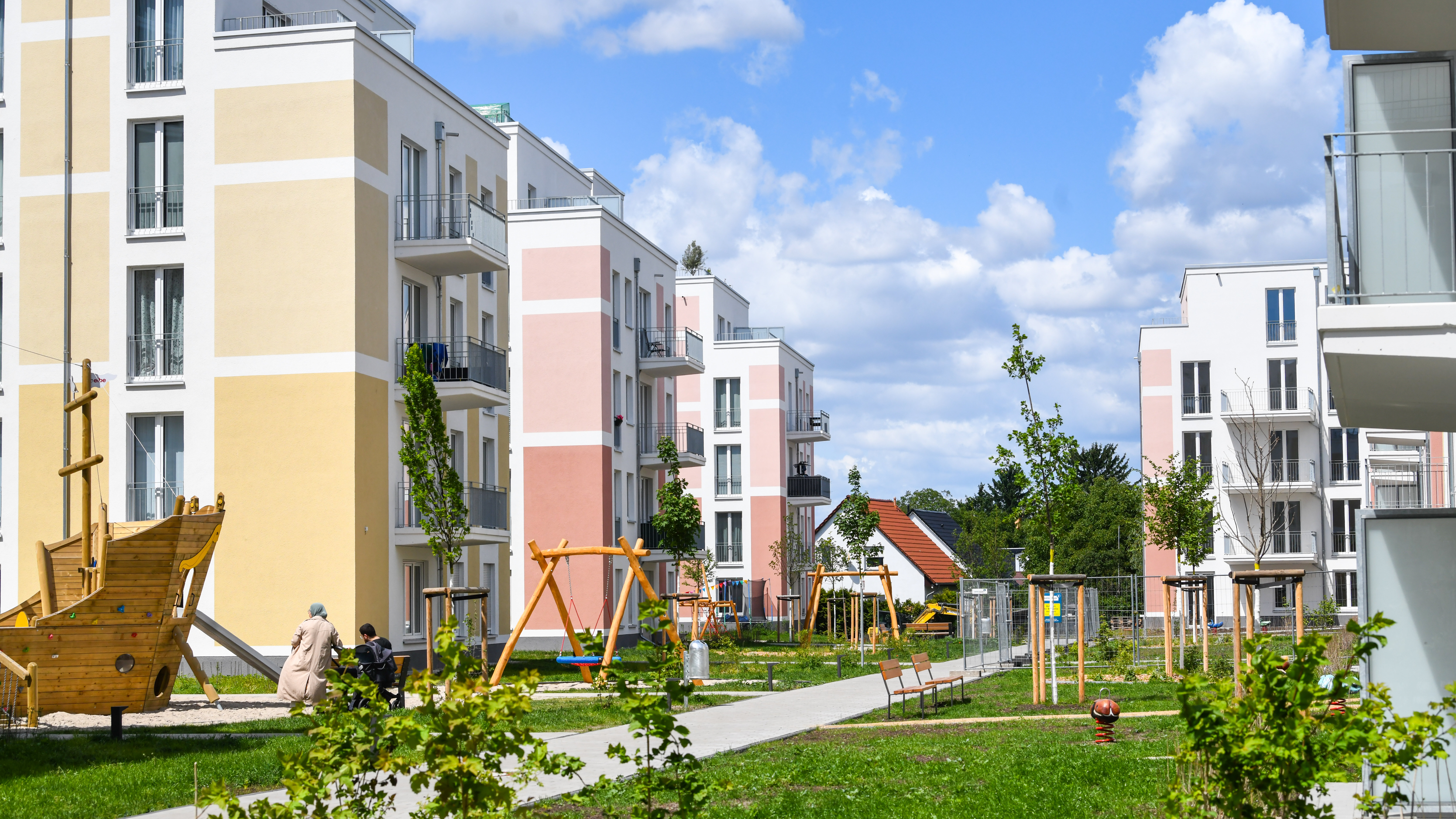 Wohnanlage mit bunten Fassaden, Spielplatz, Wegen und einigen Menschen im Gartenbereich.