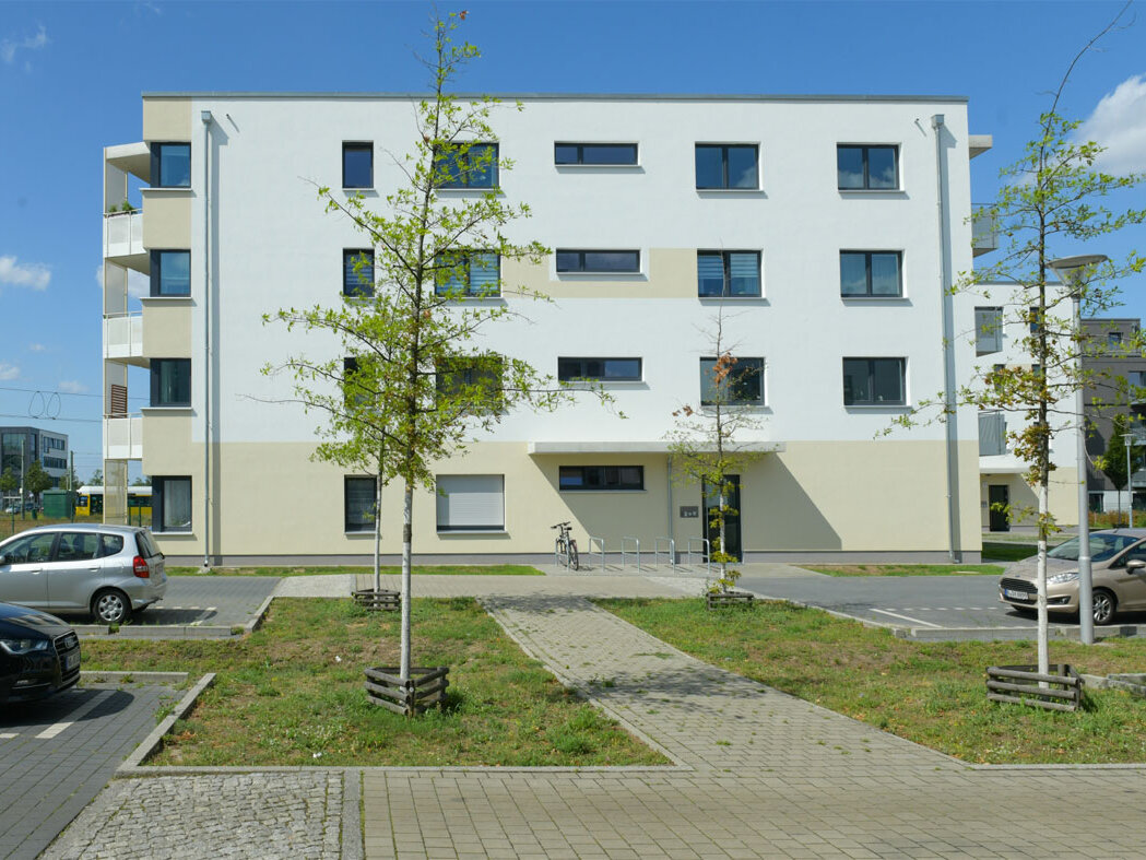 Außenansicht degewo-Neubau Wilhelm-Hoff-Straße 26 mit Wegen, Parkflächen, Grünflächen mit neu gepflanzten Bäumen im Vordergrund.