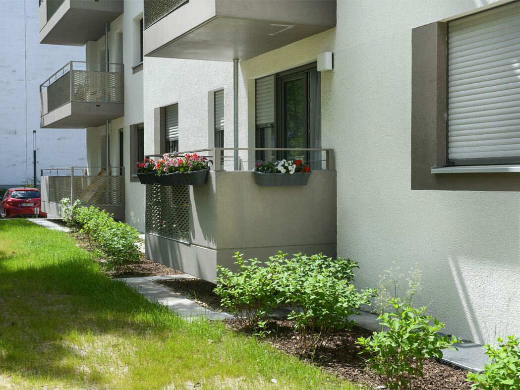 Außenansicht degewo-Neubau Theodor-Loos-Weg 15 und 15: Fassade mit Balkonen sowie Rasen und Beet im Vordergrund.
