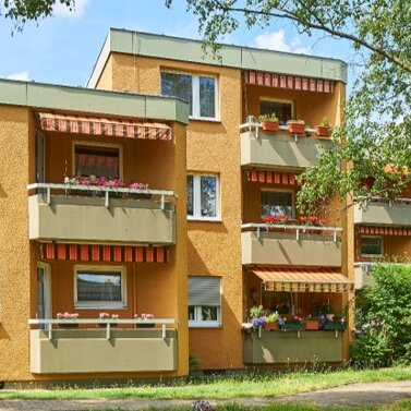 Außenaufnahme einer sanierten Wohnanlage mit gelb-orangefarbenen Fassaden und begrünten Außenbereichen. Mehrere Balkone sind bepflanzt.