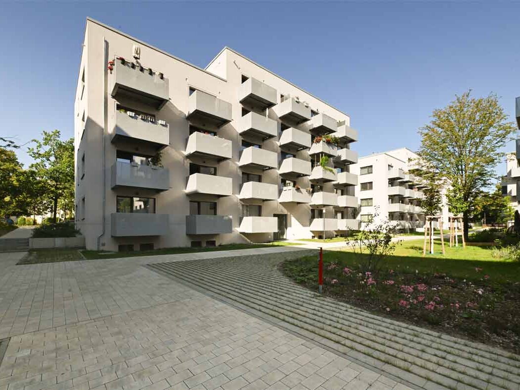 Außenansicht degewo-Neubau Malteserstraße 64: Rückseite mit gepflastertem Weg und Beet im Vordergrund.