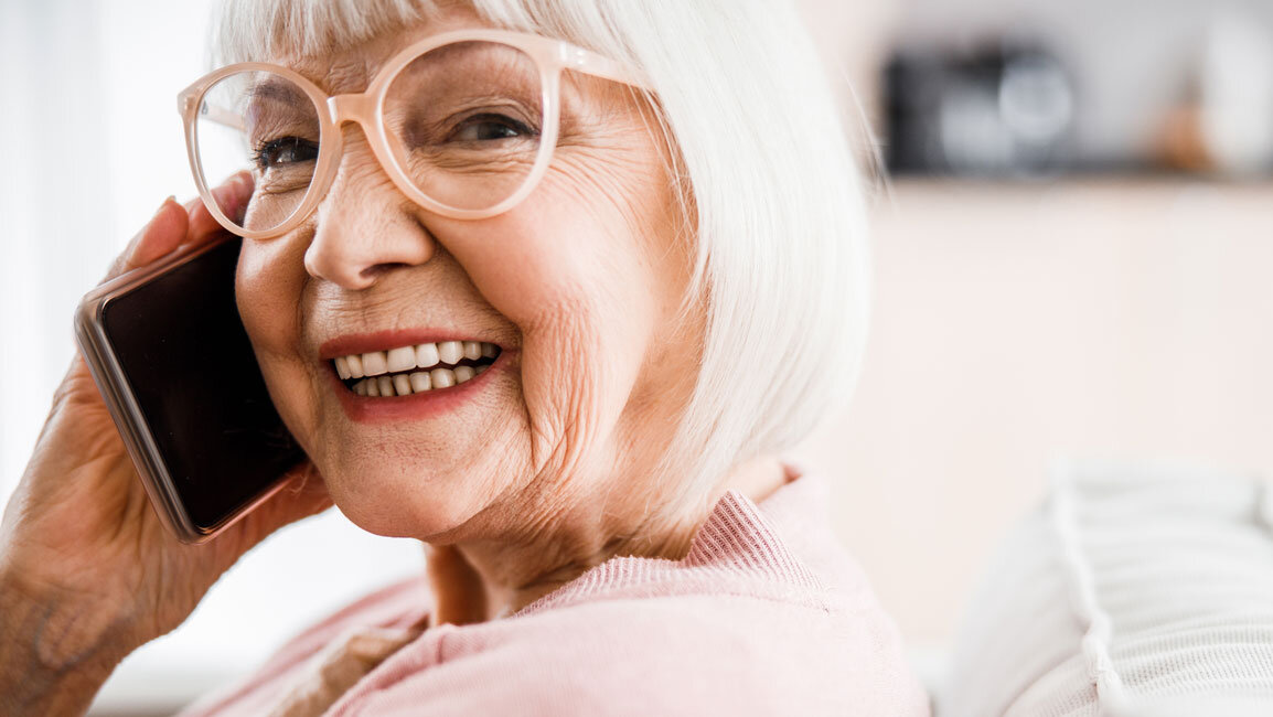 Eine ältere Frau lächelt in die Kamera während sie telefoniert. 