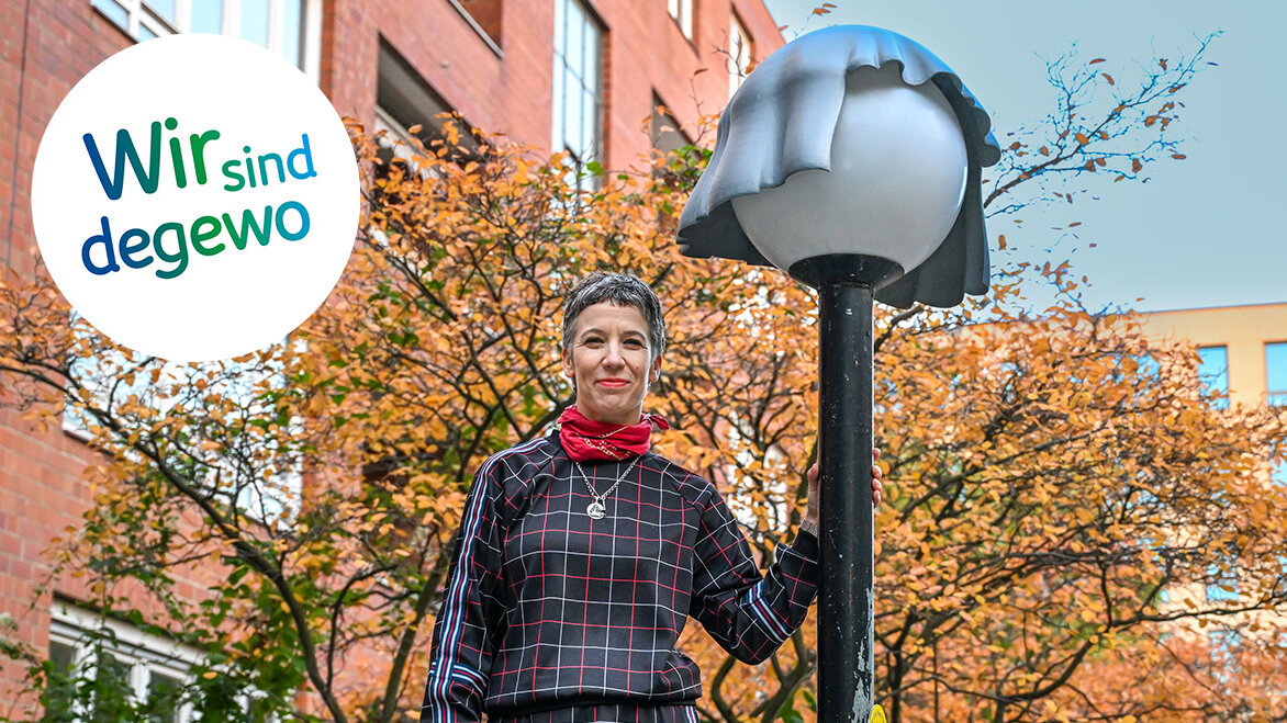 Frau steht an einer Laterne gelehnt. Die Laterne trägt eine Mütze.