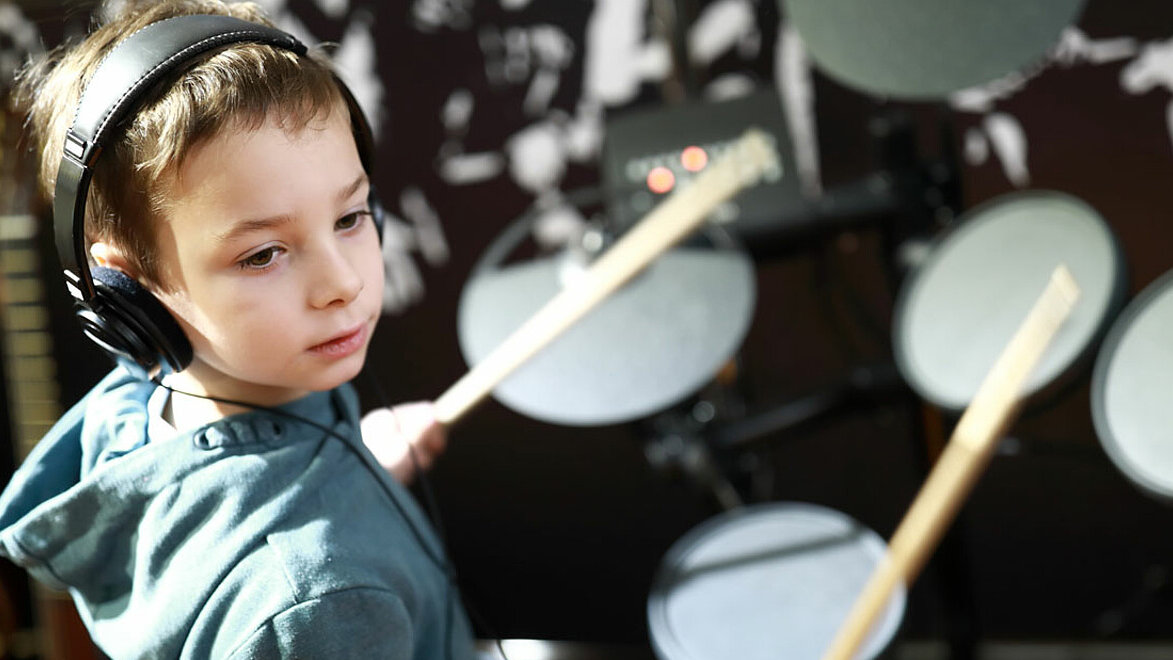 Ein Junge trägt Kopfhörer und spielt auf einem Schlagzeug.
