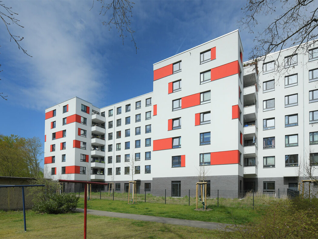 Außenansicht degewo-Neubau An der Wuhlheide 112 bis 116: Hofseite mit Grünflächen, Weg, Maschendrahtzaun, neu gepflanzten Bäumen und Wäscheleinen im Vordergrund.