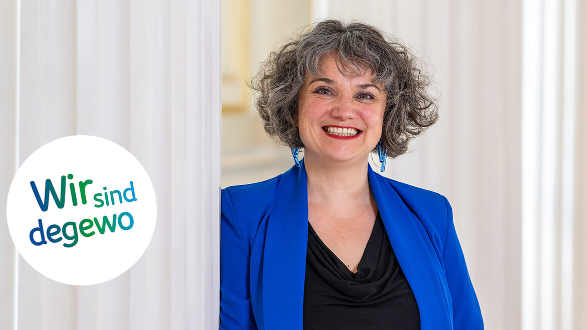 Eine Frau lächelt freundlich in die Kamera und lehnt dabei an einer hellen Säule aus Stein.