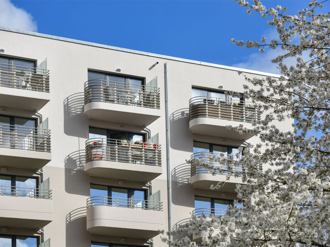 Außenansicht degewo-Neubau Venusstraße 28: Fassade mit Balkonen, rechts im Vordergrund blühender Baum.
