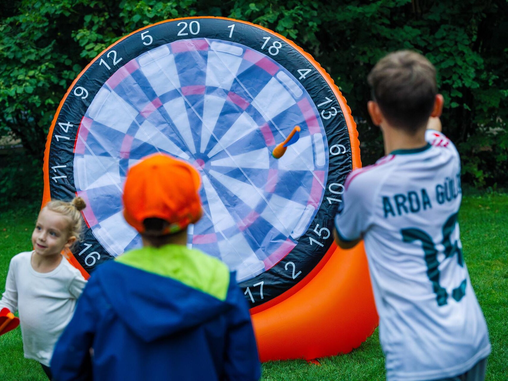 Kinder spielen auf einer Wiese an einer aufblasbaren Dartscheibe und werfen Klettbälle auf die nummerierten Zielfelder.