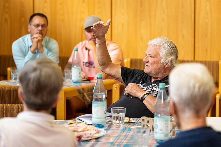 Mehrere Mietende sitzen an einem Tisch. Ein Mieter stellt den Mitarbeitenden von degewo eine Frage.