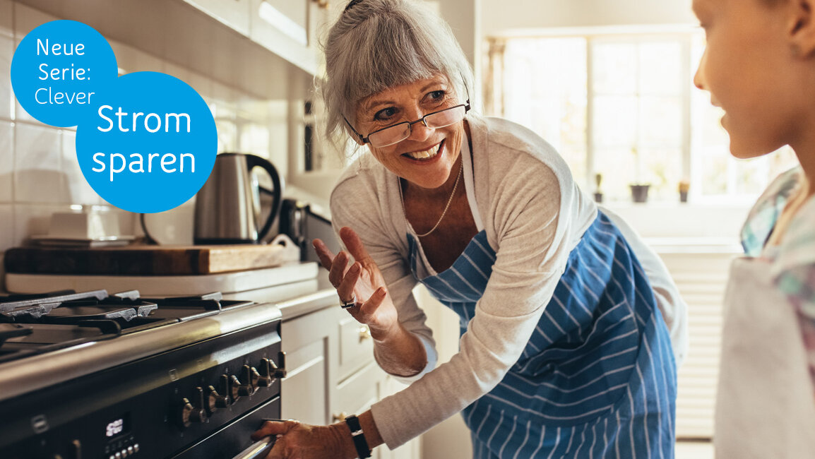 Seniorin öffnet einen Ofen. Ein Mädchen schaut dabei zu.