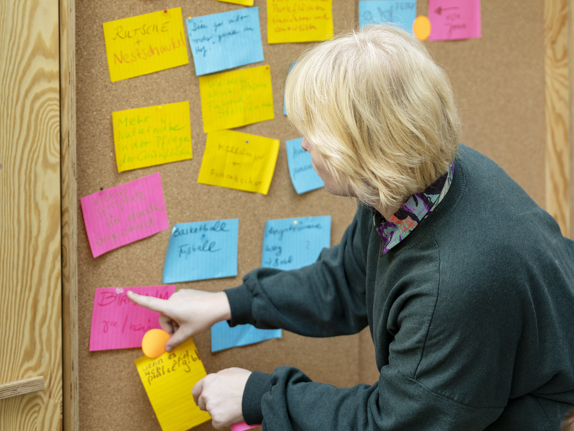 Besucherin pinnt eine weitere Idee an eine Pinnwand mit zahlreichen farbigen Notizzetteln zur Umgestaltung des Brunnenhofs.