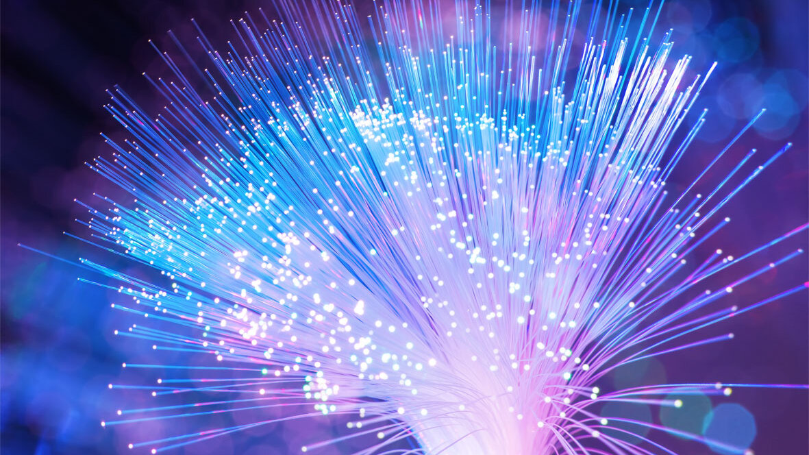 Nahaufnahme leuchtender optischer Fasern in Blau- und Violetttönen, die ein abstraktes Licht- und Linienmuster bilden.