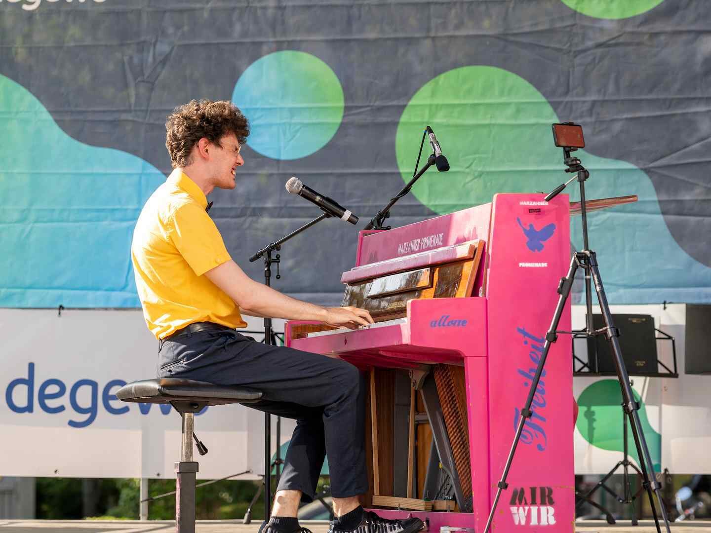 Ein junger Mann sitzt auf einer Bühne und spielt an einem pinkfarbenem Piano.