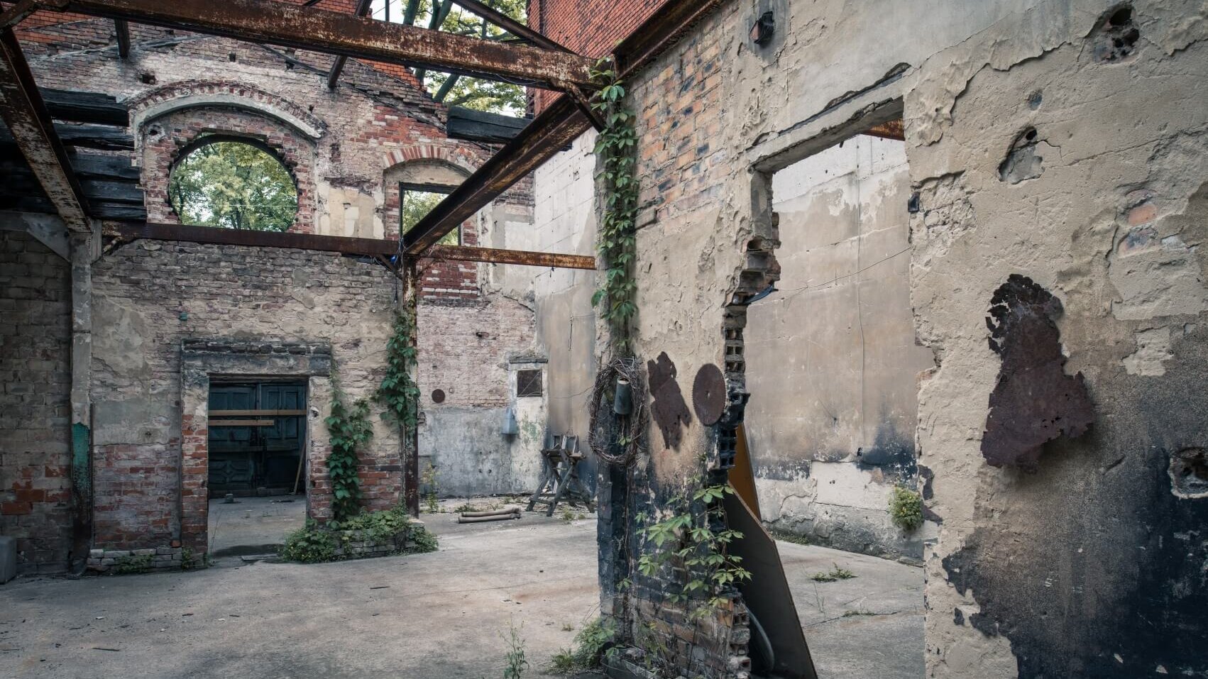Eine verfallene Backsteinruine mit offenen Mauern, Stahlträgern und überwucherter Vegetation zeigt den historischen Zustand eines Gebäudes der Wiesenburg.