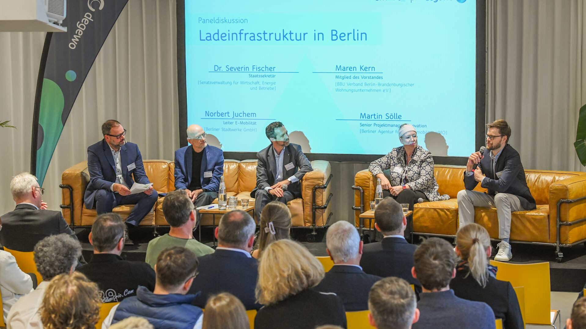 Auf der Bühne sitzen fünf Menschen auf zwei Sofas und führen eine Diskussion. Das Publikum sitzt davor und hört zu.