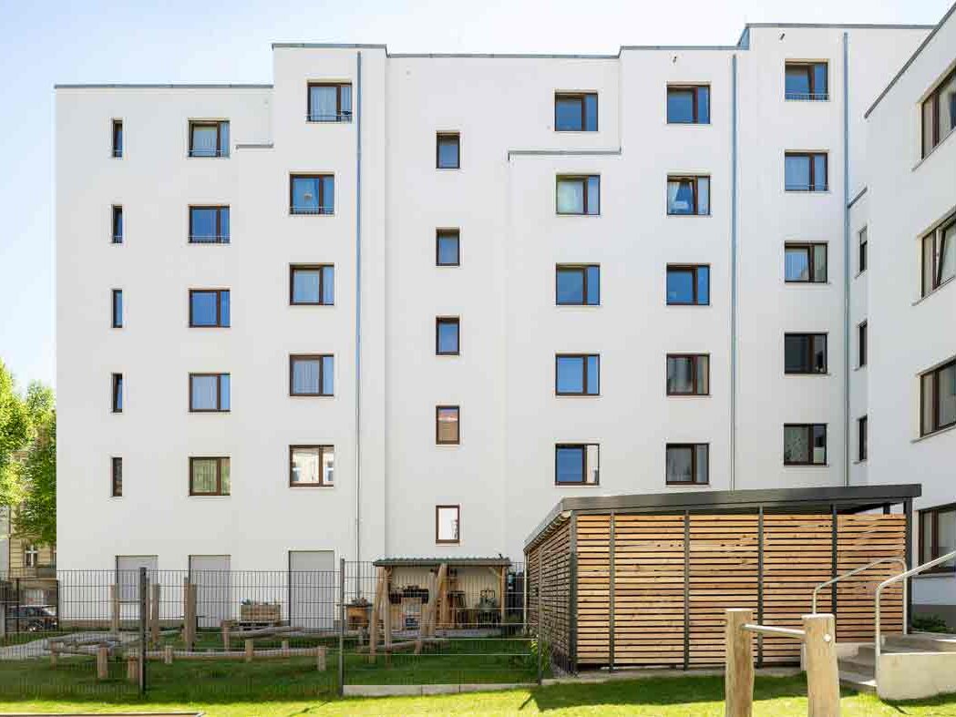 Außenansicht degewo-Neubau Glasoer Straße 3 mit Rasen und eingezäuntem Spielplatz im Vordergrund im Vordergrund.