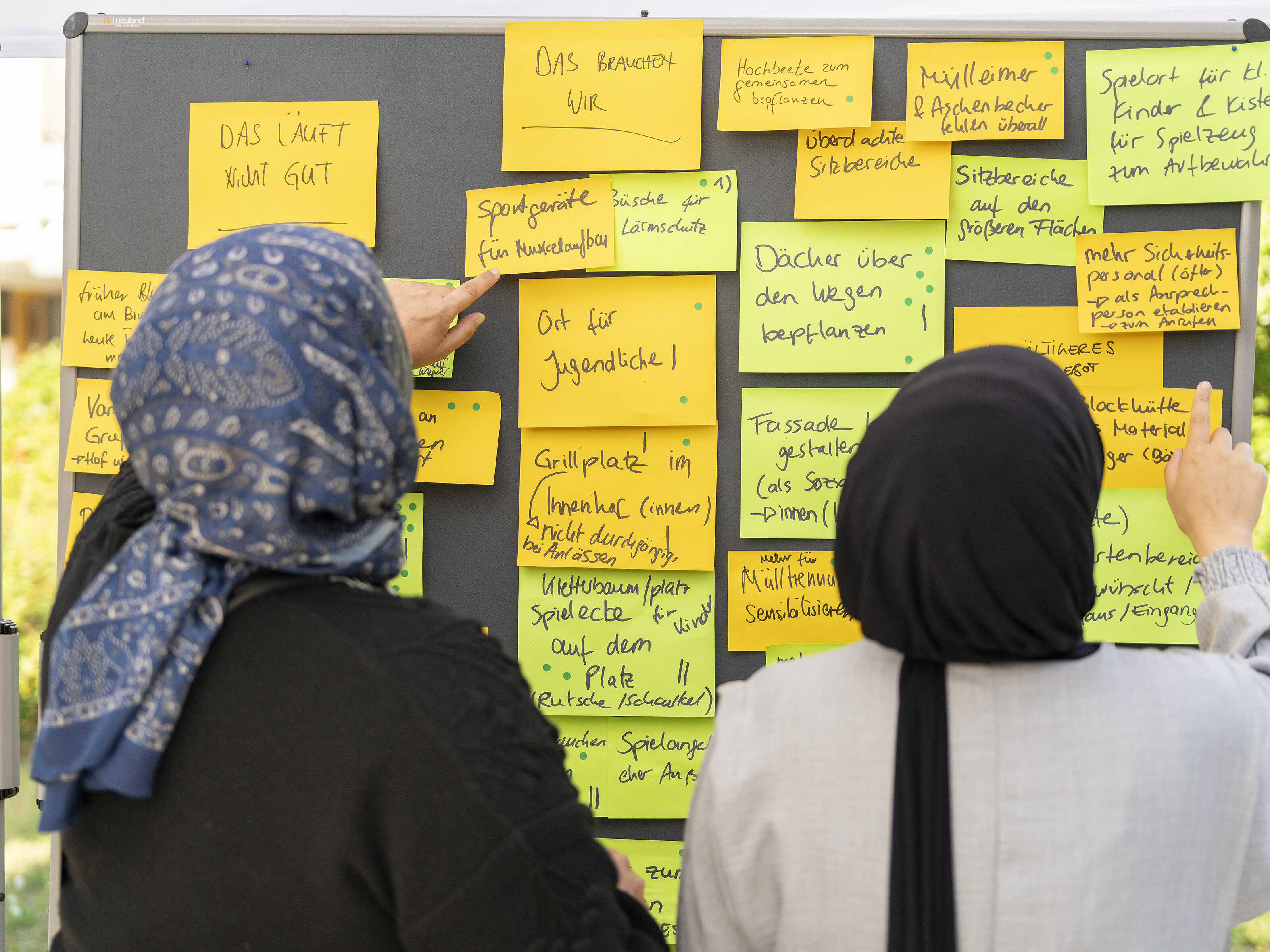 Teilnehmerinnen befestigen handschriftliche Ideen und Vorschläge auf gelben Haftnotizen an einer Pinnwand.