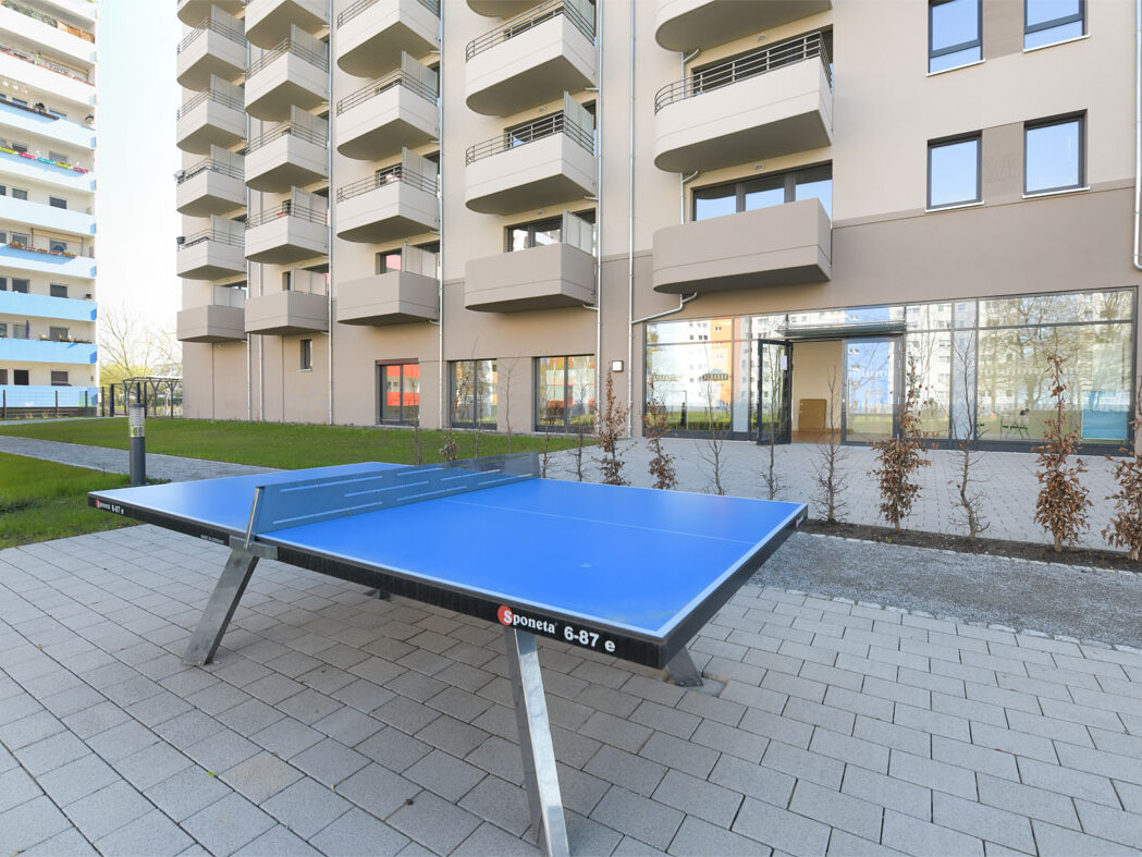 Außenansicht degewo-Neubau Venusstraße 28 mit Tischtennisplatte auf gepflasterter Fläche im Vordergrund.